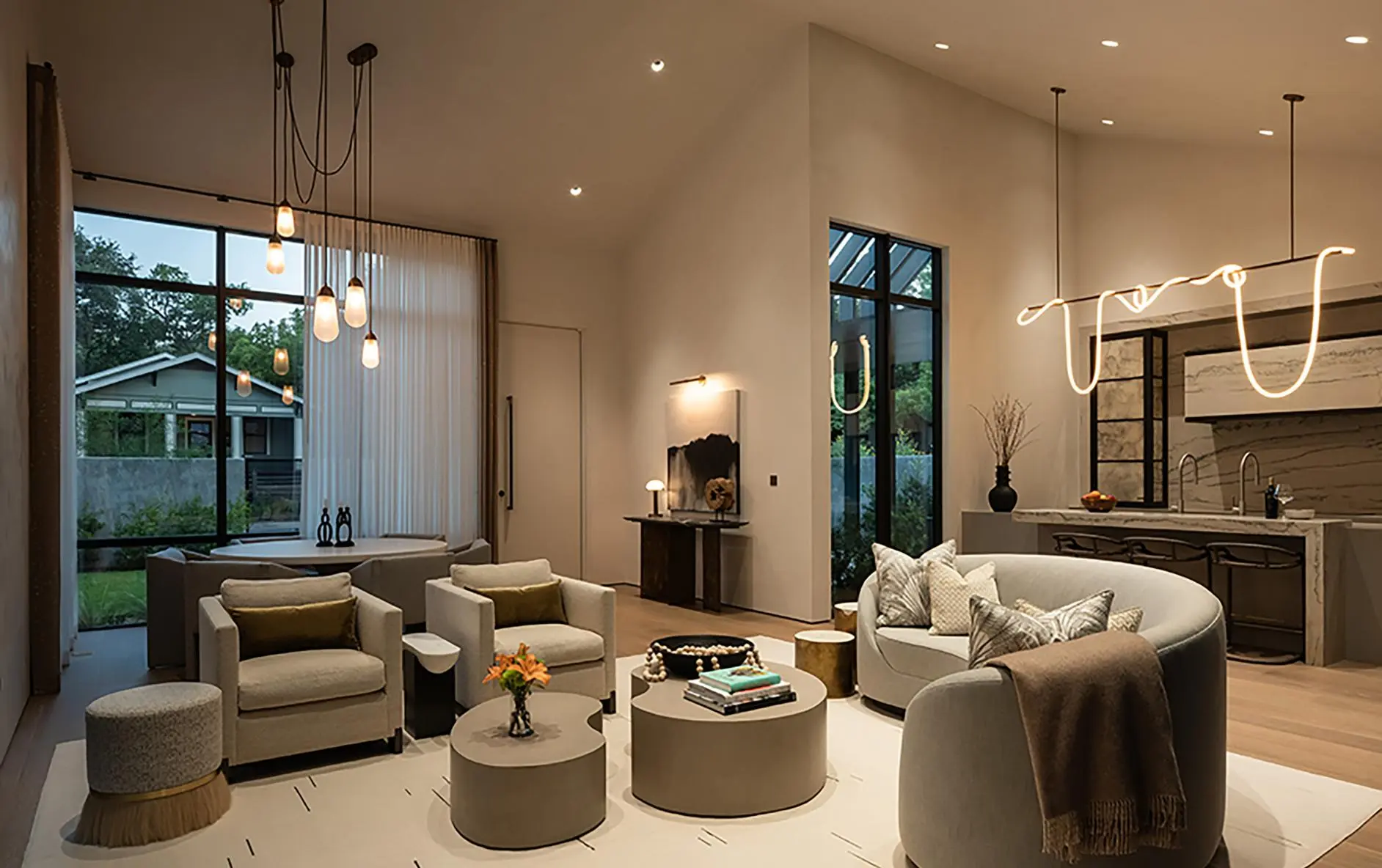 Modern living room in the evening with recessed lights, pendants, and a lit sculptural fixture over the kitchen island